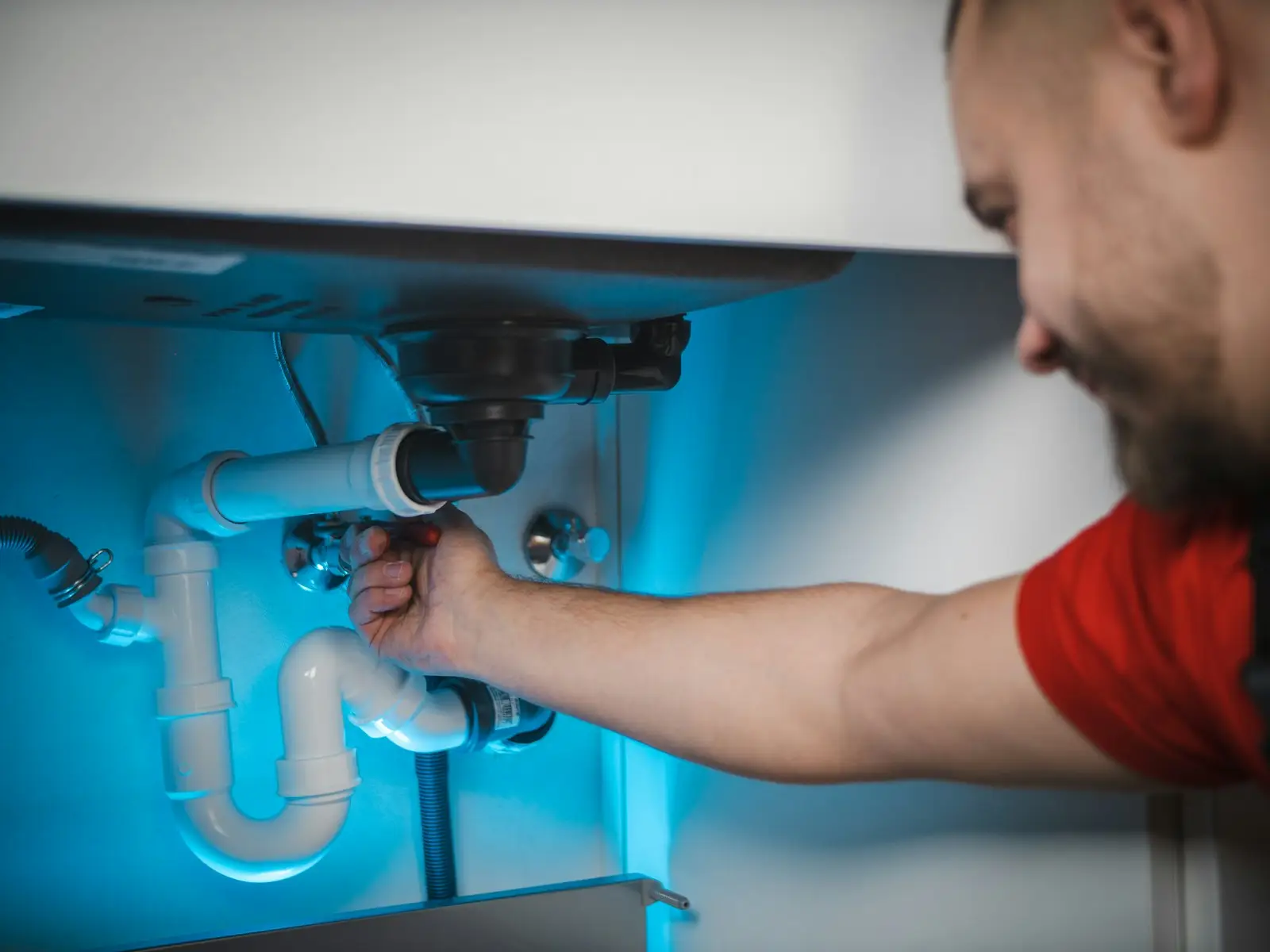 A plumber working on pipes under a sink